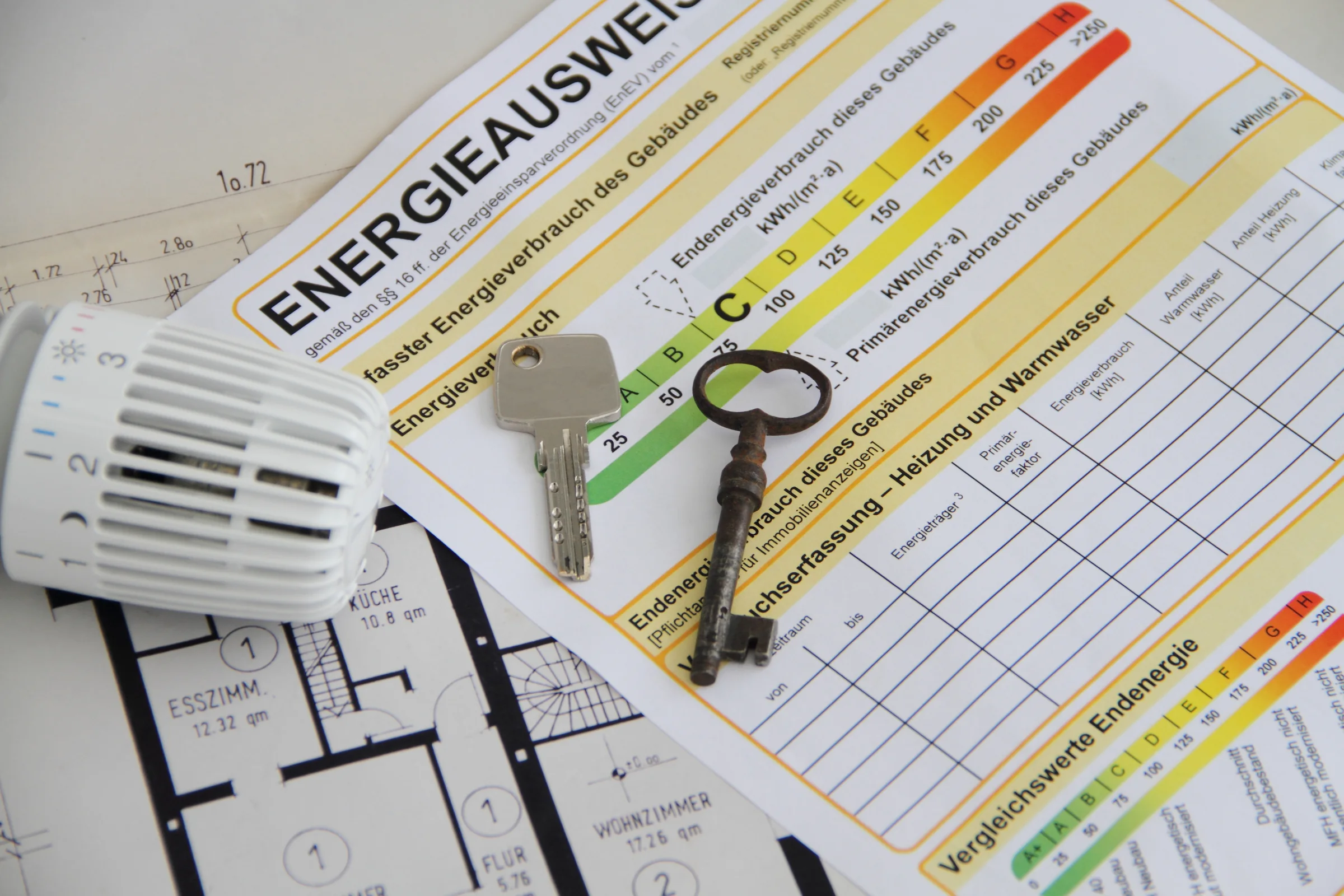 Ein Energieausweis mit Farbskala, daneben Schlüssel, Thermostatkopf und ein Grundriss